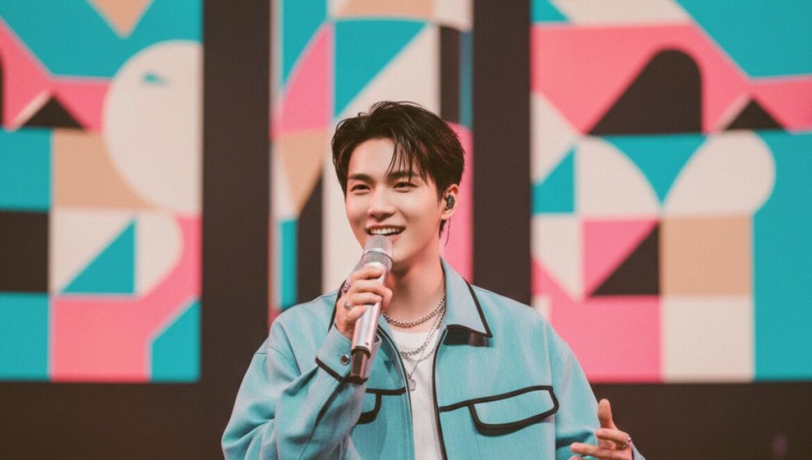 Lee Junho anuncia fan meeting por Asia de Typhoon Family: fechas, ciudades y por qué esto importa al fandom hispano Actor coreano en escenario interior, micrófono en mano, sonriendo y saludando a fans con pantallas de fondo.