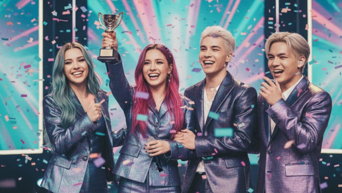 AHOF gana su 2º win con Pinocchio en Show Champion: cómo un grupo emergente venció a gigantes y cambió el juego Grupo de idols celebrando en un escenario con confeti, sosteniendo un trofeo ante pantallas LED.