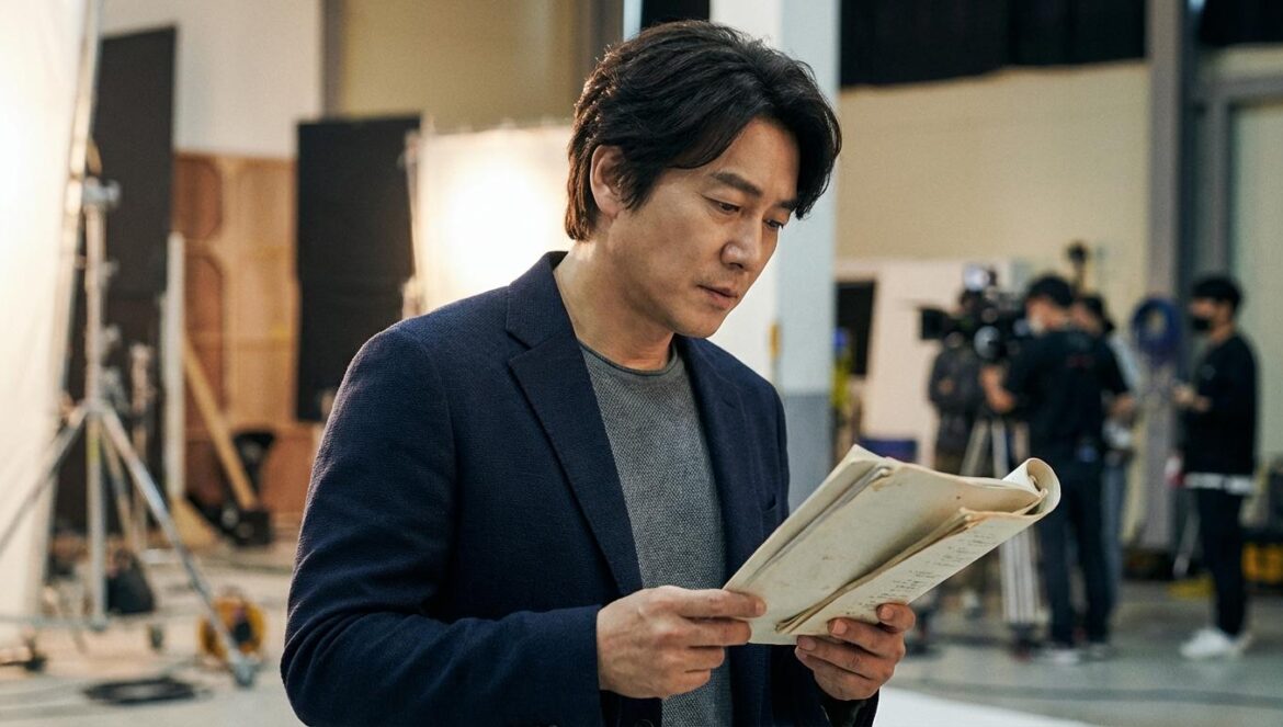 Yoon KyungHo salta de robaescenas a héroe total en el K‑drama “Kim BuJang” Actor coreano de mediana edad sosteniendo un guion en un set de rodaje desenfocado.