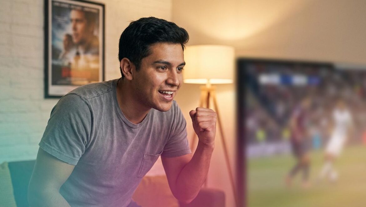 Highlander y el grito “solo puede quedar uno”: del cine al deporte competitivo Joven aficionado al deporte reacciona emocionado frente al televisor mientras se intuye un póster de película al fondo.