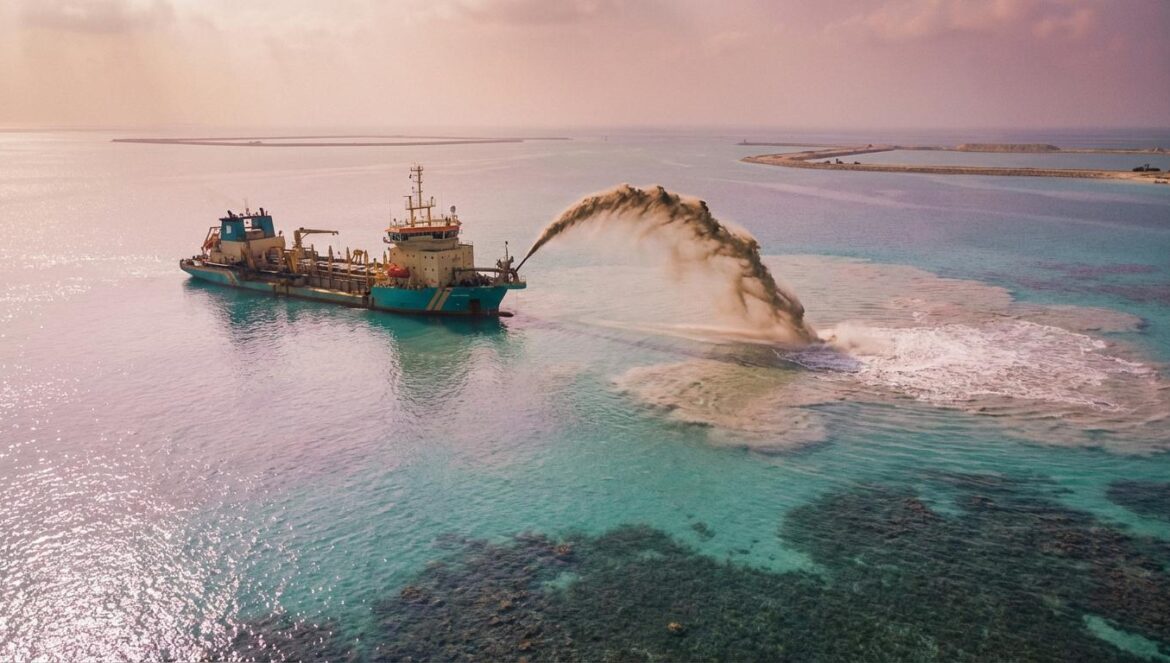 Islas artificiales de China: el timelapse que convierte arena en poder (y en ansiedad regional) Un barco de dragado expulsa arena al mar turquesa, formando una isla artificial con una nube de sedimentos y diques en el horizonte