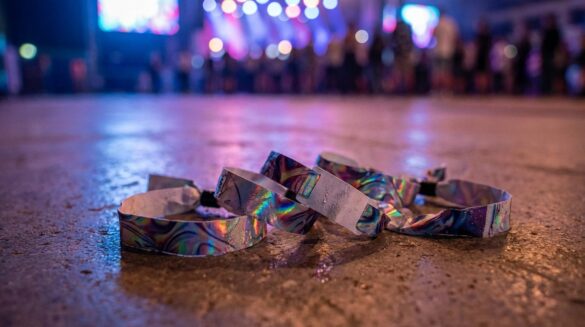 Pulseras holográficas de concierto sobre suelo de cemento, con luces de escenario desenfocadas al fondo y ambiente nocturno