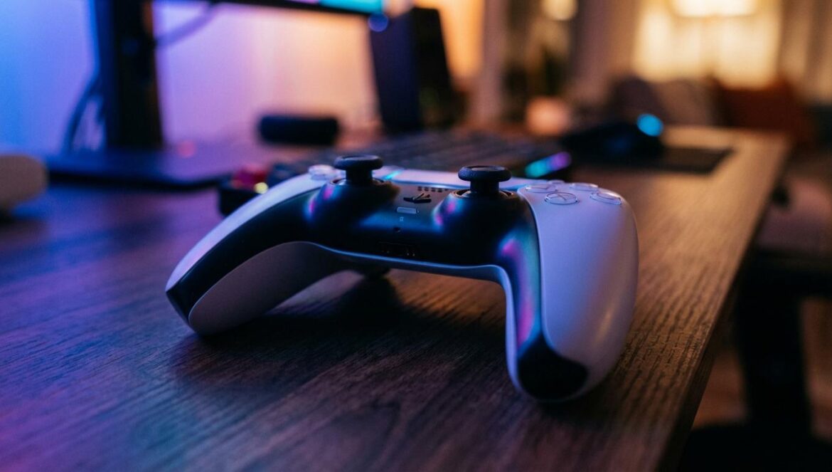 Sony State of Play de febrero: El regreso de los mitos Primer plano de un mando de consola moderno sobre una mesa de madera con iluminación ambiental azul de estilo gamer.