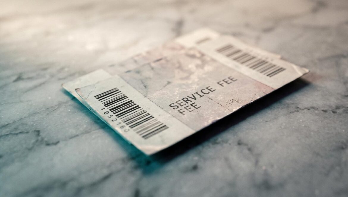 Live Nation y el DOJ: un acuerdo que deja a los fans fuera Primer plano de entradas de concierto desgastadas sobre una superficie de mármol frío, con énfasis en el texto de las comisiones de servicio bajo luz fluorescente.