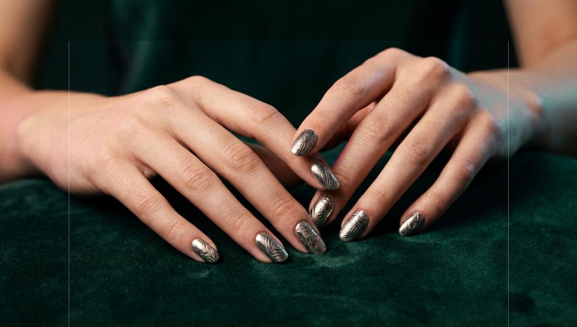 Yves lanza NAIL: el giro de 180 grados a su carrera solista Primer plano de manos con arte de uñas metálico sobre terciopelo verde oscuro, con iluminación dramática y sombras profundas estilo editorial.