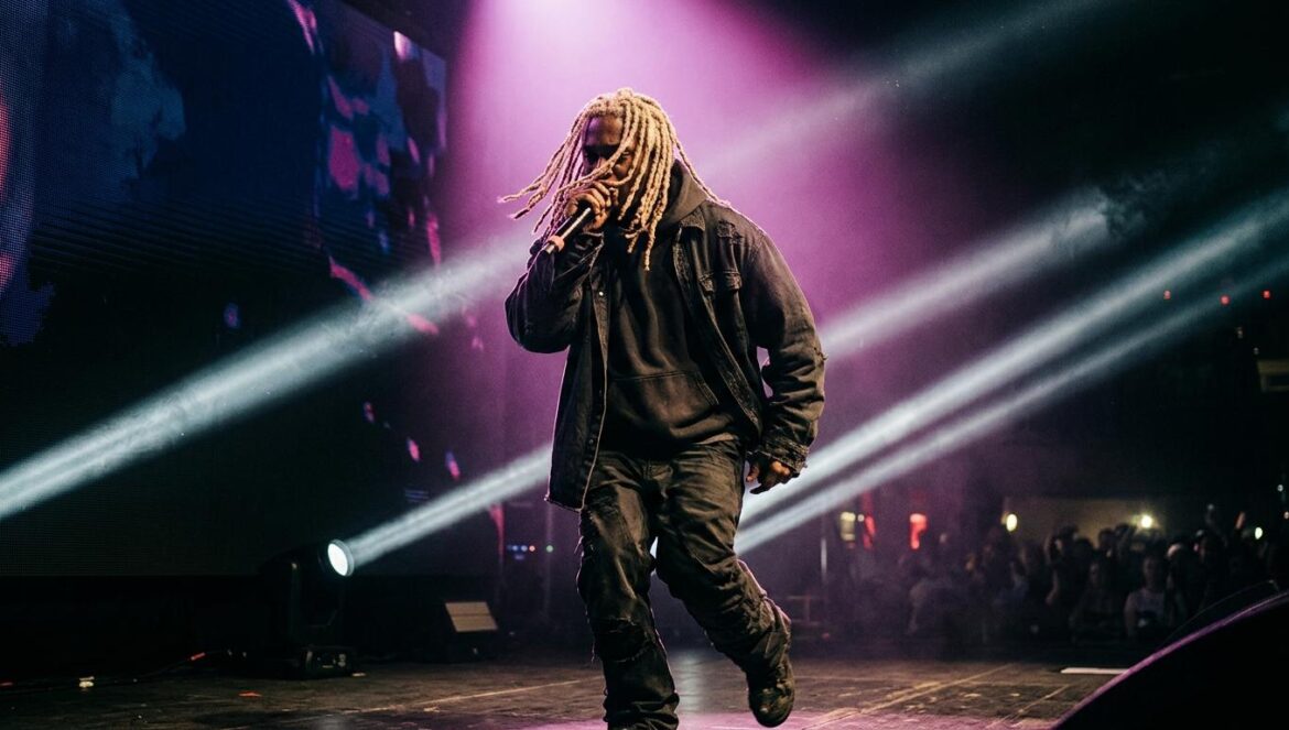 bleood en concierto: el espejismo del rage rap en 2026 Un rapero de espaldas con rastas decoloradas sobre el escenario de un club oscuro iluminado por potentes luces estroboscópicas blancas y magenta.