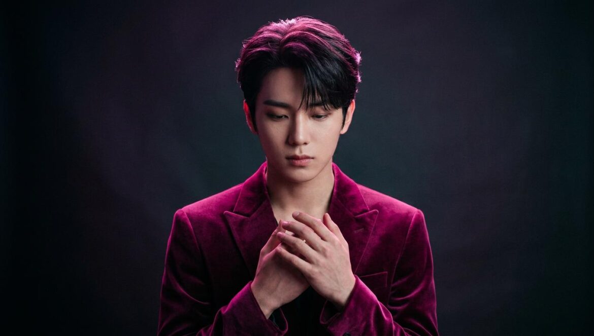 Dongyeon de POW pausa su carrera tras la pérdida de su padre Retrato de estudio minimalista de un artista de K-pop en una pose reflexiva con iluminación de fondo dramática en tonos magenta.
