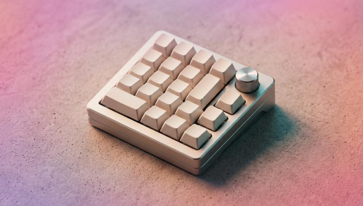 Vista en plano detalle de un teclado macro de diseño minimalista sobre una mesa de concreto con iluminación de tonos cálidos y sombras turquesa.
