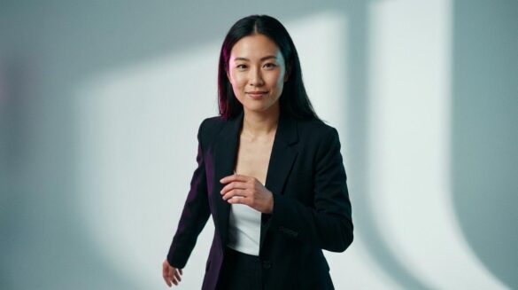Retrato de estudio de una mujer asiática con traje de sastre elegante, iluminada con tonos magenta y turquesa sobre un fondo minimalista.