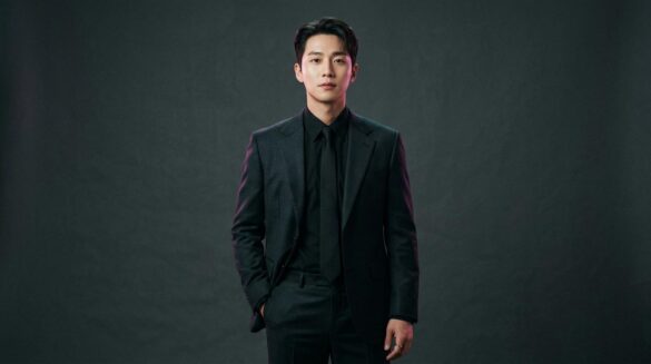 Retrato editorial de un actor coreano con traje oscuro estructurado bajo una iluminación tenue con detalles en magenta y turquesa.
