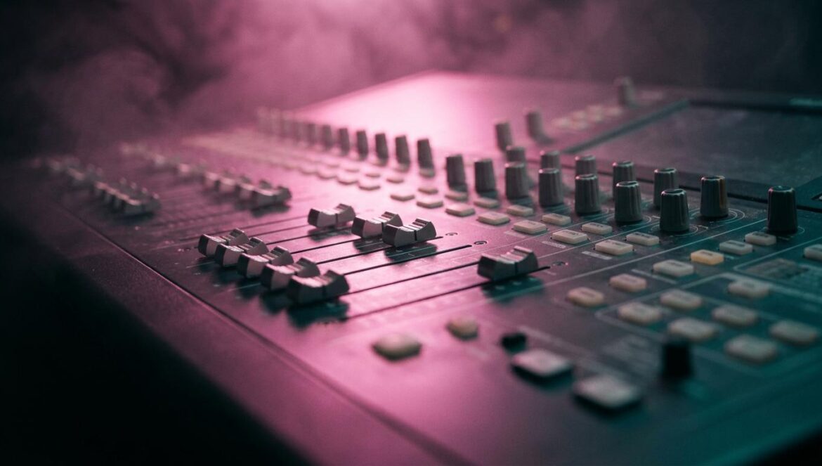 MNEK desafía al algoritmo con su nuevo álbum BULLDOZER!! Primer plano de una mesa de mezclas profesional iluminada con tonos magenta y turquesa en un estudio de grabación oscuro.
