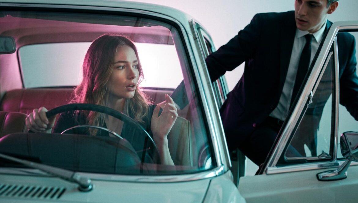 Retrato editorial de un hombre y una mujer sorprendidos dentro de un coche clásico con iluminación magenta y turquesa de estilo cinematográfico.